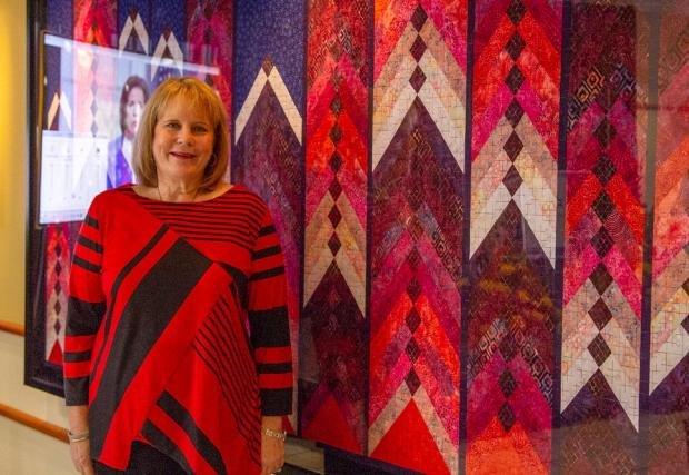 Lois DeGiulio standing in front of her homemade quilt